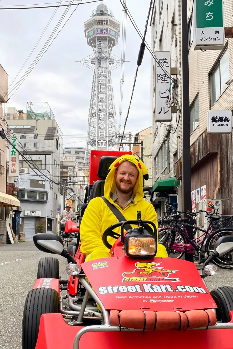 Mann im Pikachukostüm in einem Go-Kart vor dem Tsutenkaku Tower in Osaka