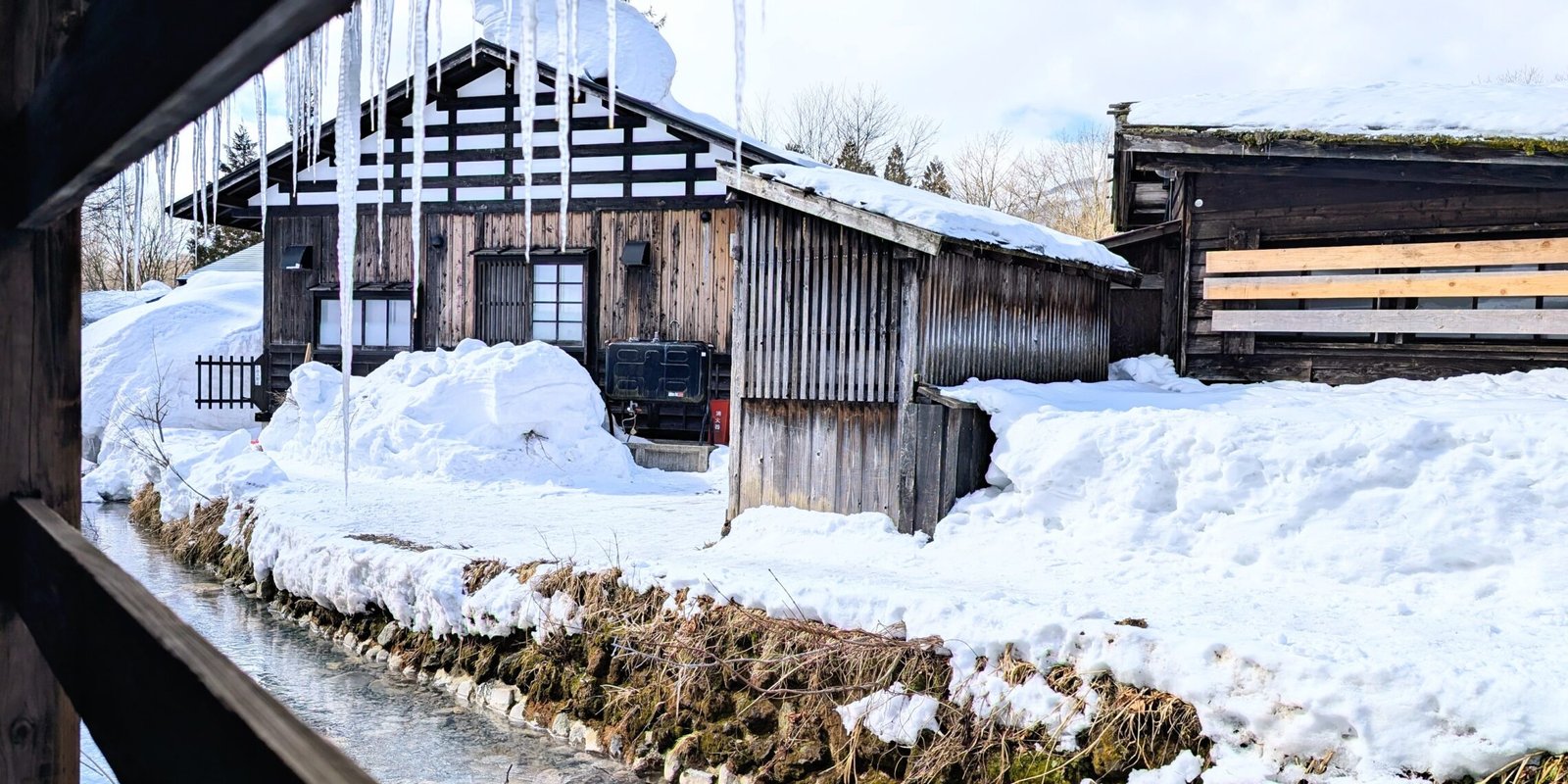 Blick aus einer Hütte im Tsurunoyu Onsen auf einen winterlichen Fluss mit Eiszapfen